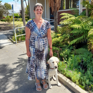 A woman standing with her guide dog, smiling for the camera.